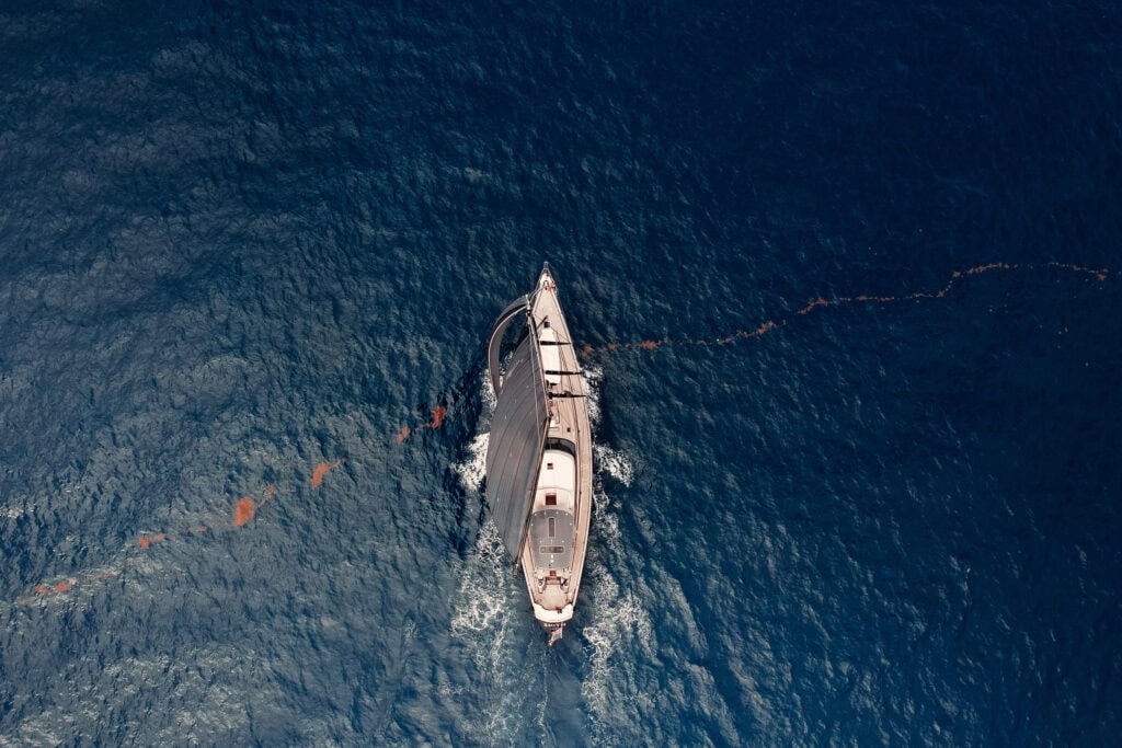 Aerial view looking down on a classic sailing yacht under power leaving a long wake