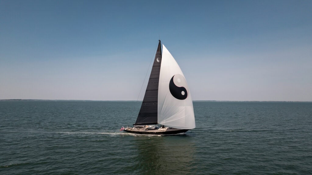 Black-hulled sloop under full sail carrying a yin-yang emblem on the mainsail