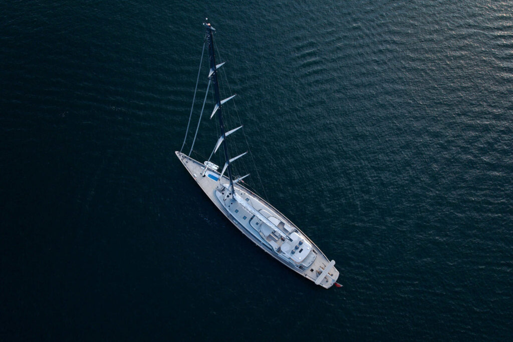 Overhead drone view of a white sailing yacht at anchor on deep blue water