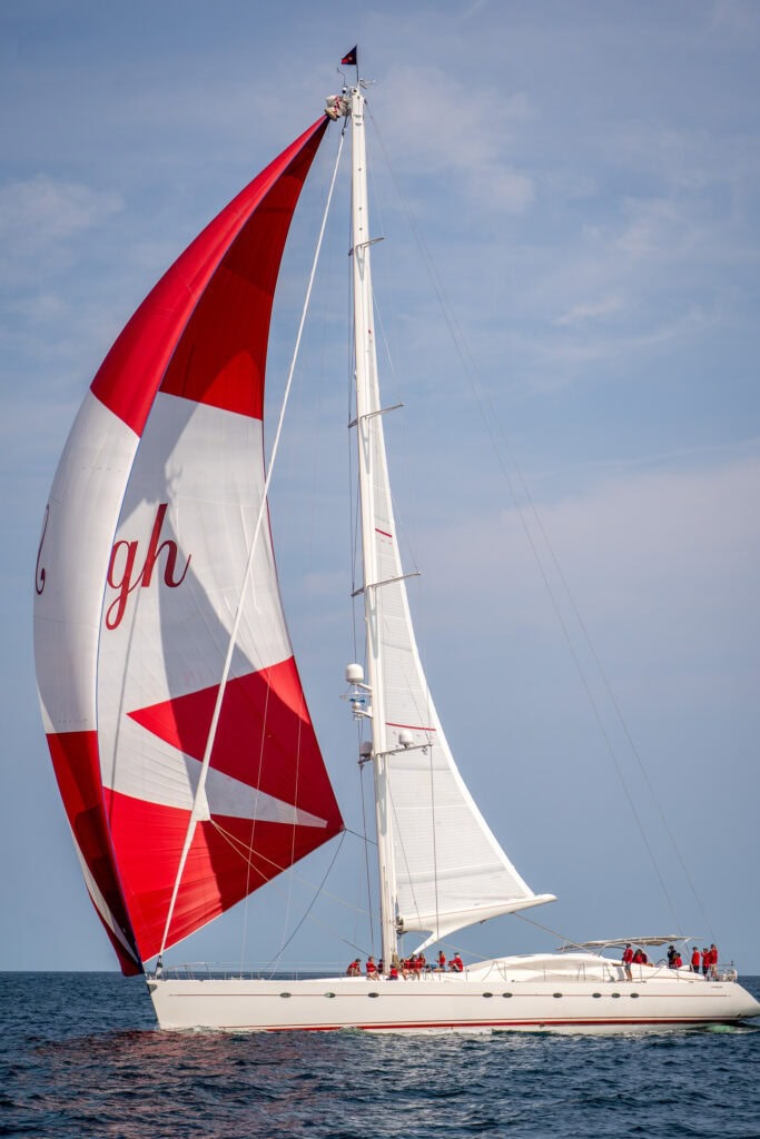 Sailing yacht running under a red and white spinnaker during a regatta