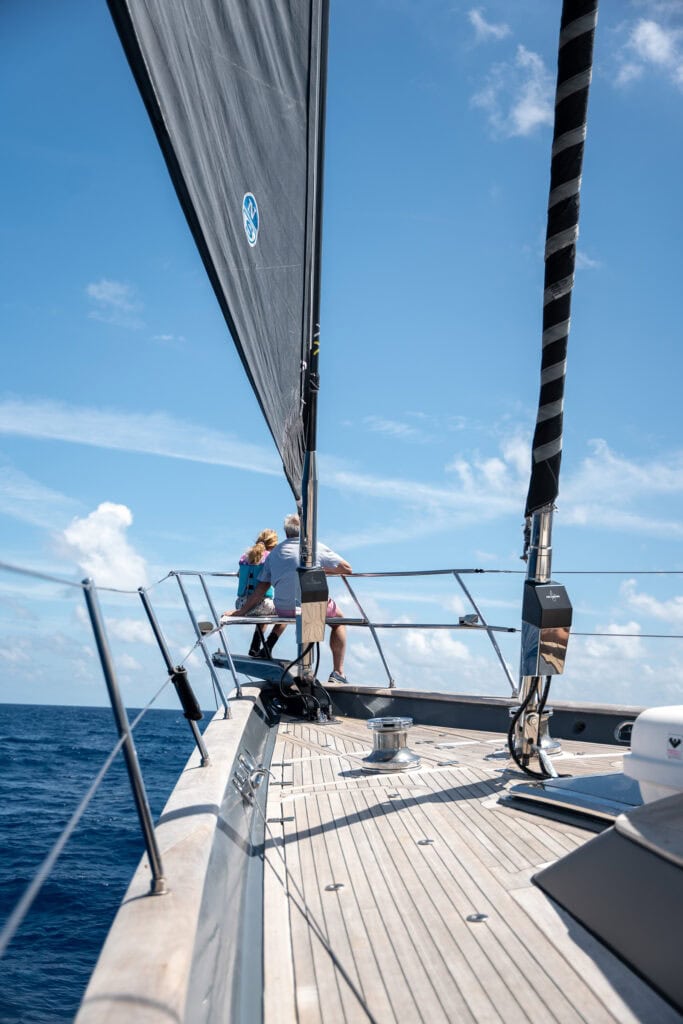 Crew working forward on the teak deck of a sailing yacht under full sail on a clear day