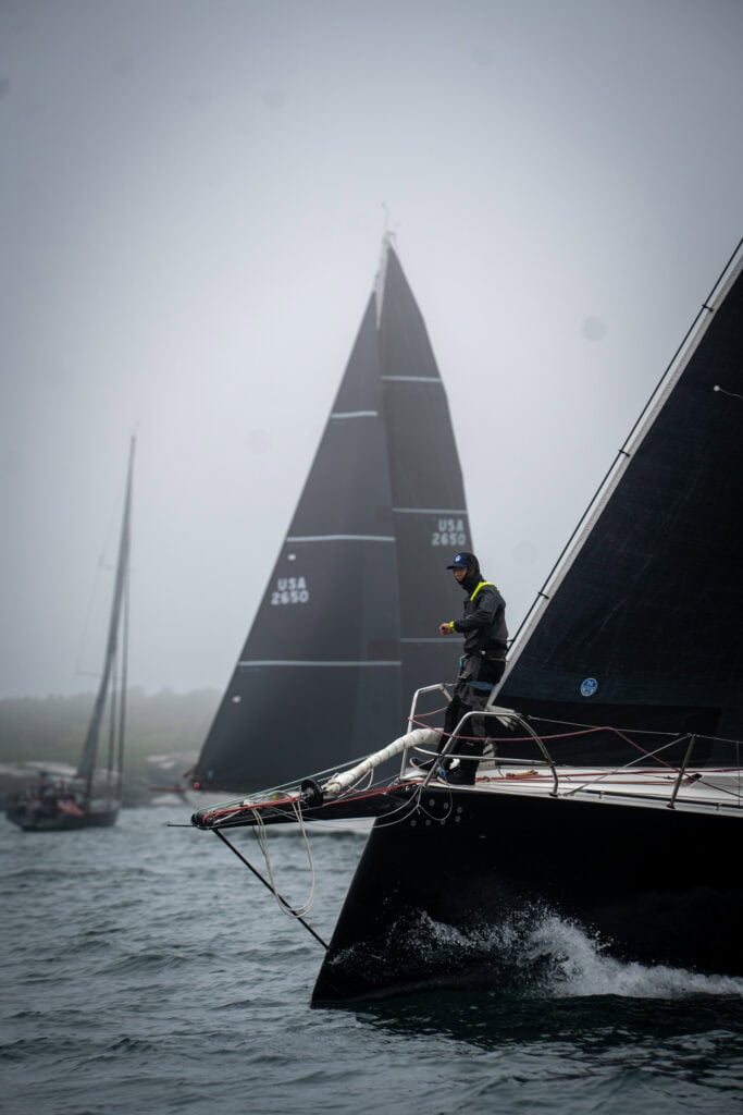 Dark racing yacht sailing in mist with a crew member working on the bow