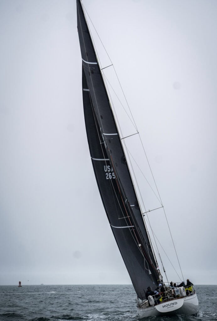 Black-hulled sloop under full sail in soft haze offshore