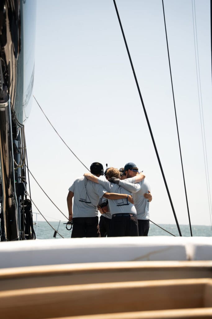 Crew in matching white shirts gathered together on the foredeck of a sailing yacht under way