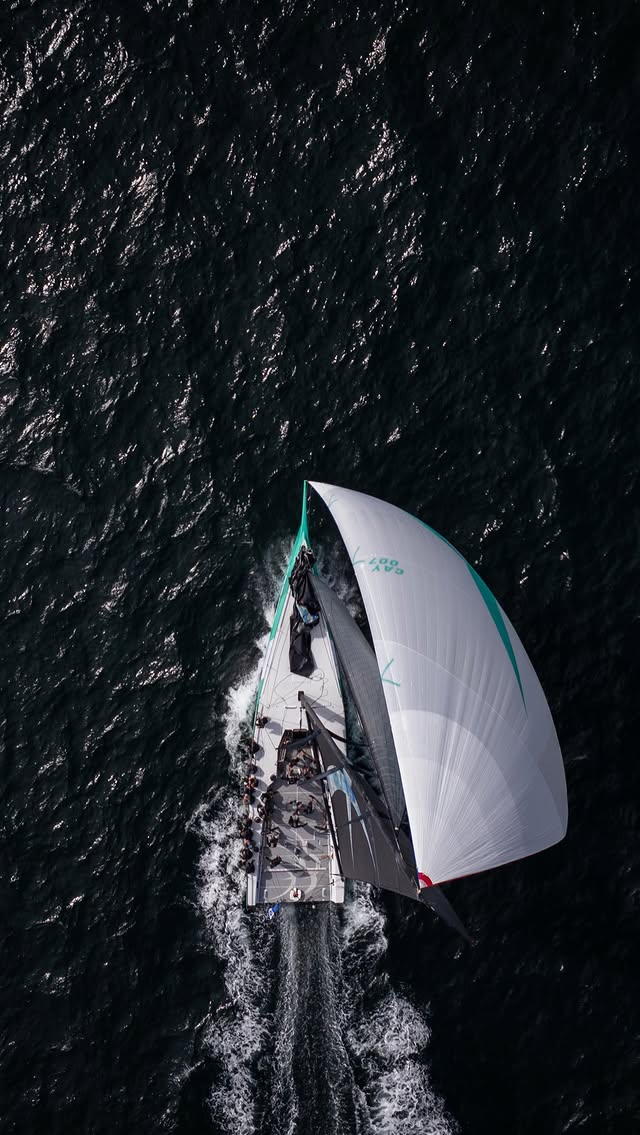 Overhead drone view of a sailing yacht running downwind under a white spinnaker with crew on deck