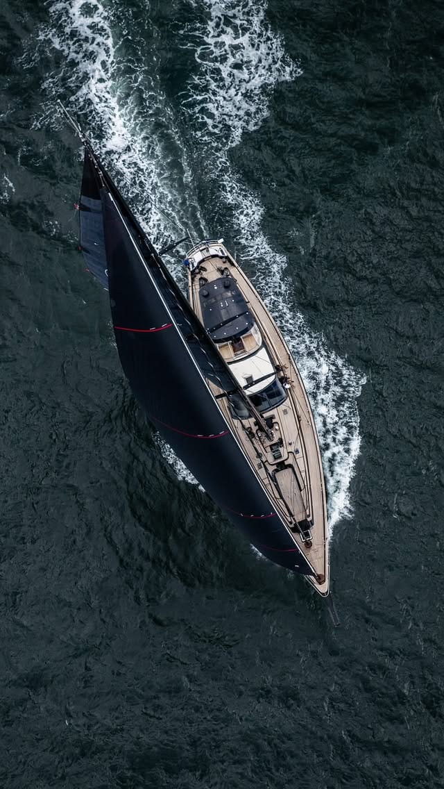 Aerial view looking down on a dark-hulled motor yacht under way, wake astern