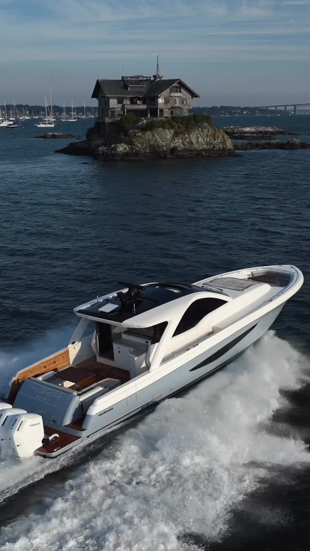 White sport tender running fast past a rocky headland and shingled house near Newport, Rhode Island