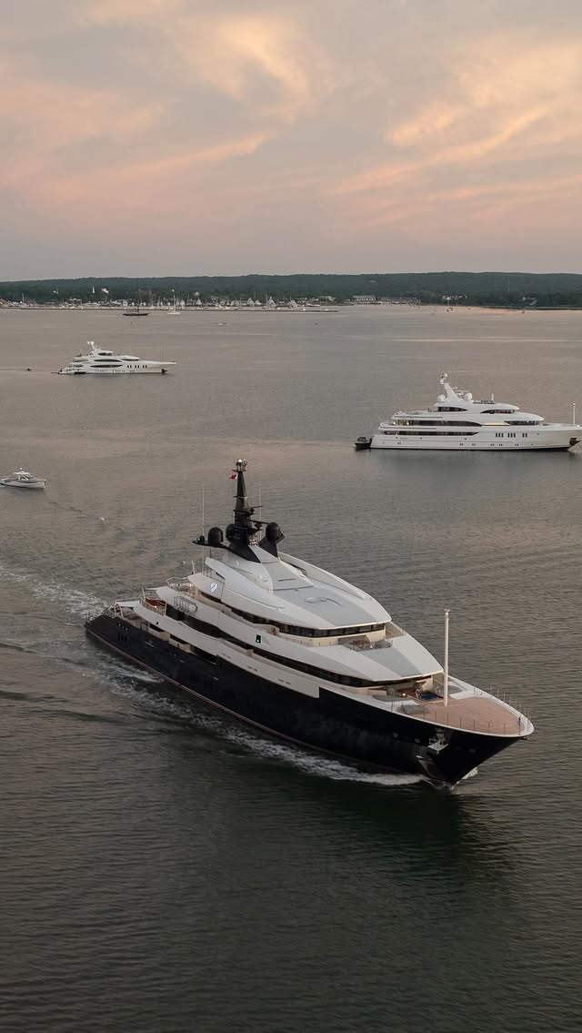 Motor yacht under way at dusk on calm water with anchored yachts behind