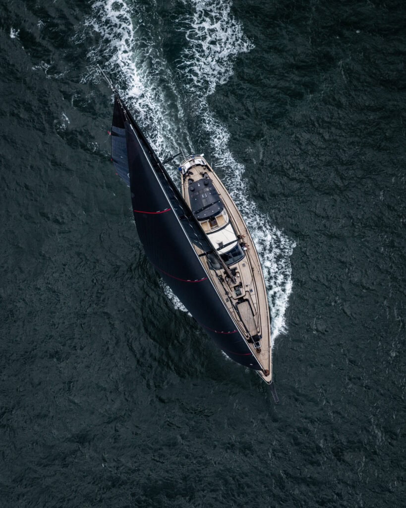 Overhead drone view of a sailing yacht under way offshore, wake trailing astern, on a yacht delivery